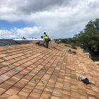 Workers installing shingles on a rooftop under a cloudy sky.