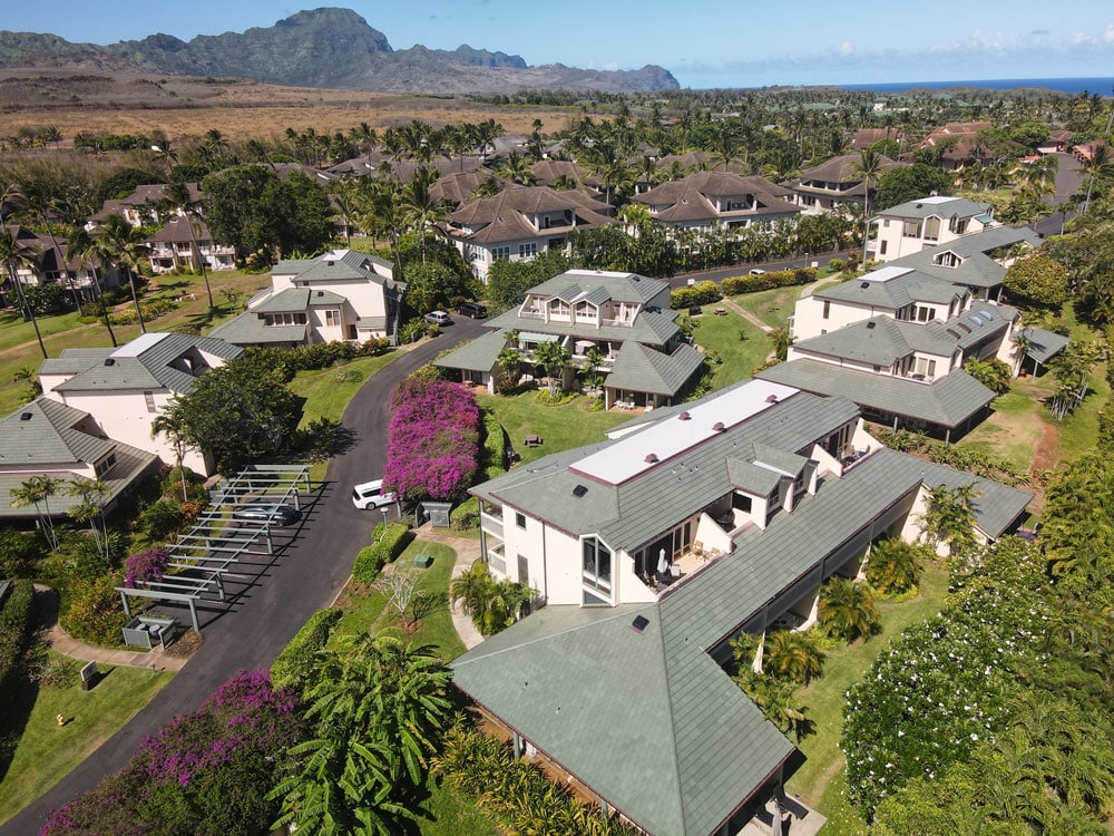 Aerial view of a residential area with lush greenery and mountain backdrop.